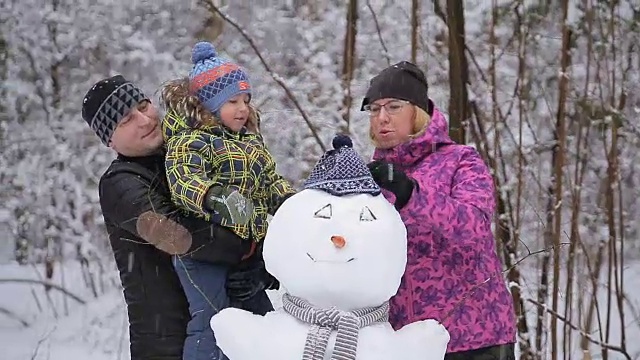 快乐的小家庭在清新的雪中玩耍，在美丽阳光明媚的冬日户外堆雪人视频素材