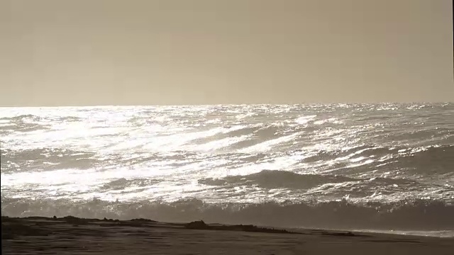 在一个阳光明媚的日子里，海浪翻滚着涌向沙滩视频素材