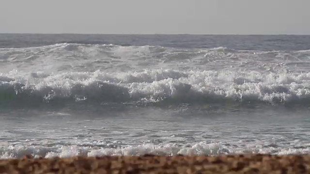 在一个阳光明媚的日子里，海浪翻滚着涌向沙滩视频素材