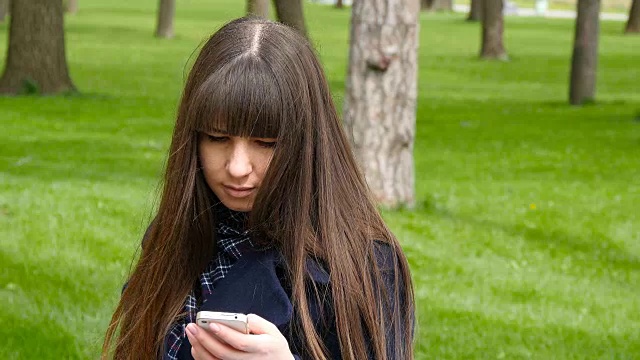 美丽的女人使用手机在户外的公园细节。年轻迷人的快乐女孩放松在一个城市公园和使用手机。她看起来很高兴，很满足视频素材