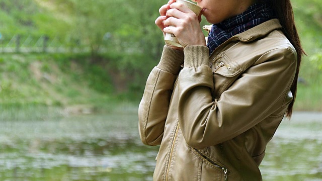 公园里的女孩用一次性杯子喝外卖咖啡。女人端着一杯热茶视频素材