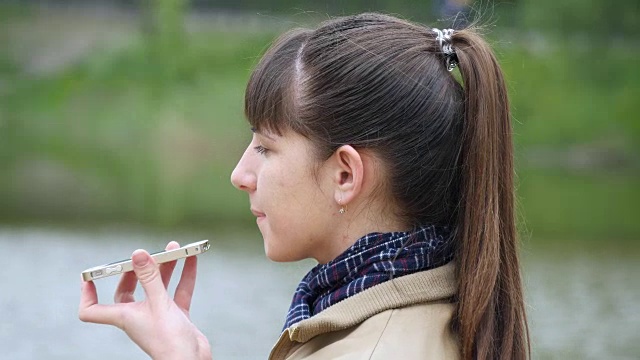 一名年轻女子站在河堤上打电话。春天，女孩在室外用智能手机说话。特写镜头视频素材