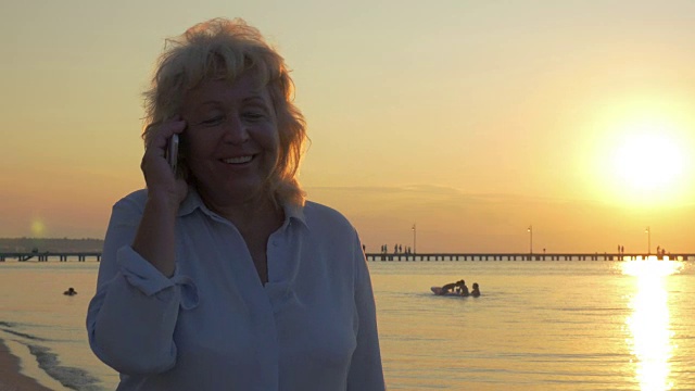 老女人在日落时分的海滩上打电话视频素材