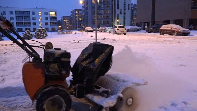 在冬天的晚上，吹雪机清理住屋停车场的人行道。视频素材