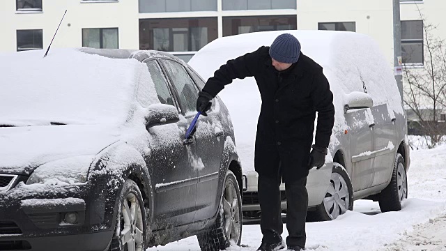 一名男子在居住区用刷子清理汽车上的积雪。视频素材