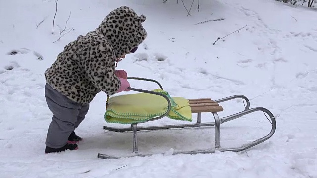 快乐的宝贝女孩在冬季公园的雪地上推雪橇。手持。视频素材