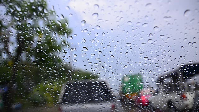 近距离拍摄雨滴在汽车车窗玻璃和模糊的交通环境下，阴雨昏暗的背景视频素材