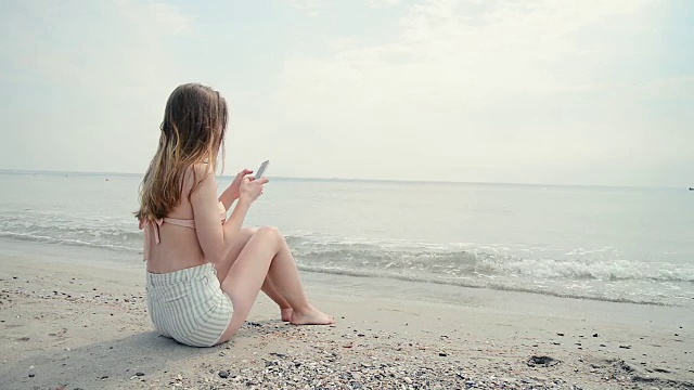 年轻女子在沙滩上用手机拍照视频素材