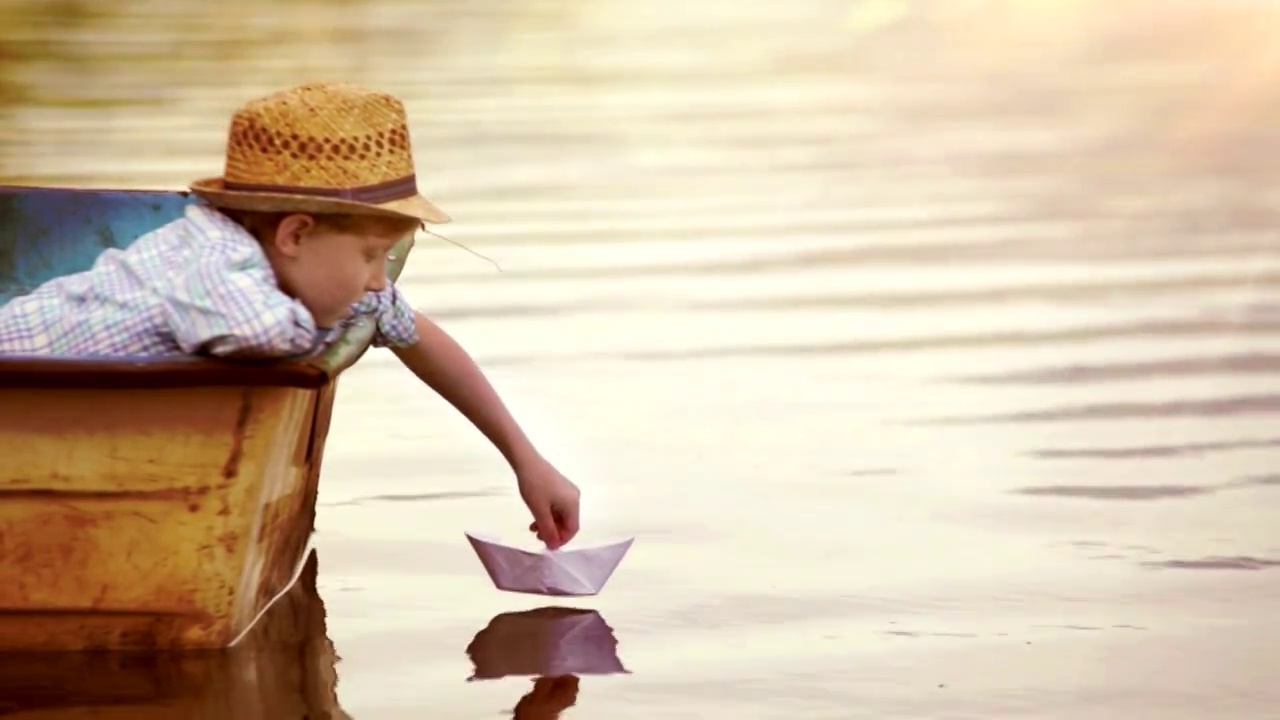 男孩把一只纸船放在水面上，吹着风让它飞走视频素材