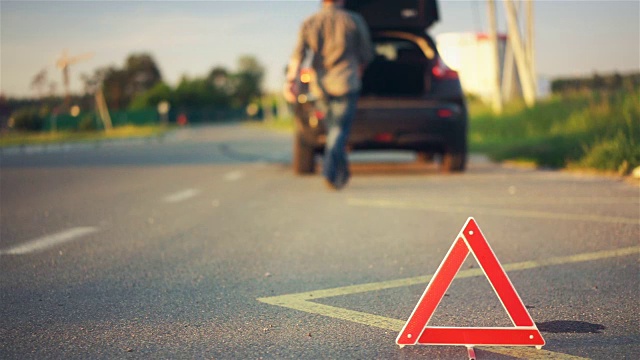 道路上的红色三角形警告，汽车抛锚，司机在后备箱里找工具视频素材