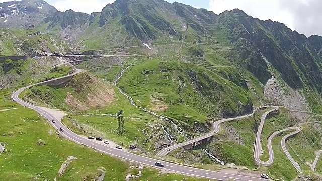 风景优美的公路跨越了高海拔的山脊，汽车在许多壮观的弯道和转弯之间行驶，航拍镜头视频素材