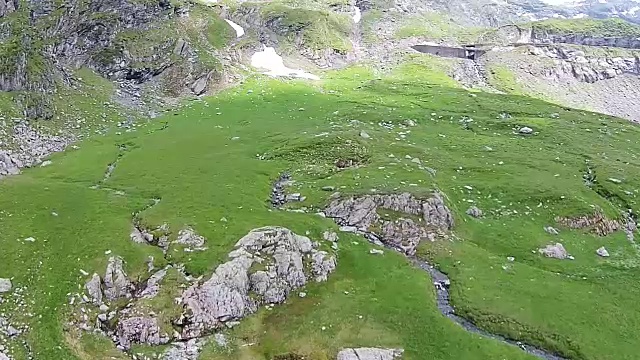 高海拔的山地高原特有的风景，以积雪融化形成的岩石和小河，陡峭的山谷和山峰为背景，航拍镜头视频素材