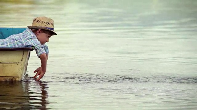 一个小男孩坐在湖中心的木船里向四周洒水视频素材