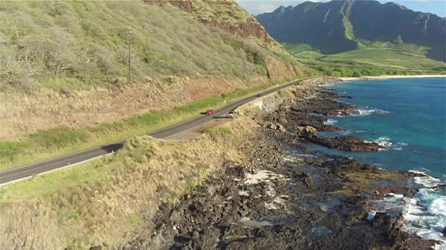 航拍:豪华红色敞篷车行驶在岩石海岸上的海岸公路上视频素材