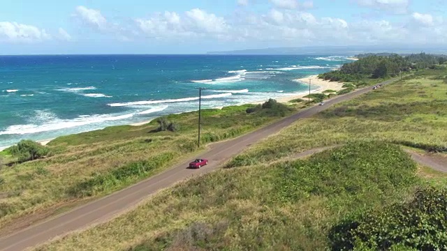 航拍:红色敞篷车沿着绿色夏威夷岛的海岸公路行驶视频素材