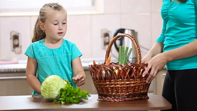 女孩帮助妈妈从篮子里拔菜视频素材