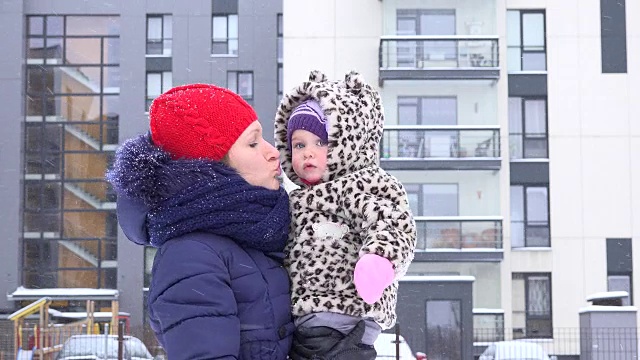 好玩的妈妈和小女孩在自家院子里享受雪花飘落的暴风雪。FullHD视频素材