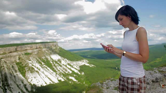 有魅力的女人用智能手机发短信，背景是群山视频素材