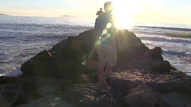 日落时分，十几岁的男孩在加州海滩上和岩石上散步视频素材