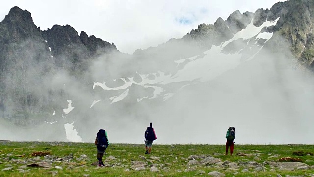 在Kavkaz地区，一群背着徒步背包的游客来到高耸的雪山中视频素材