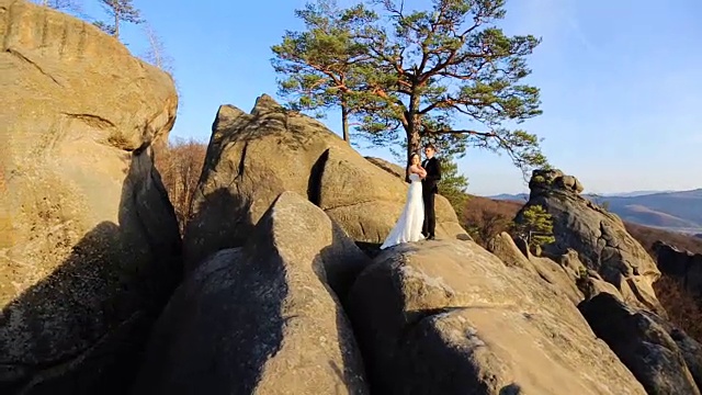 美丽的新娘和优雅时尚的新郎拥抱在岩石上的夕阳山的背景视频素材