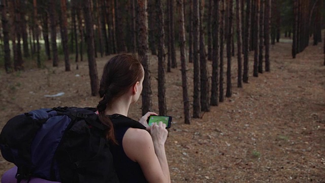 在美丽的野生森林里，背包女游客使用智能手机上的导航应用程序。旅行的概念。换绿屏准备视频素材