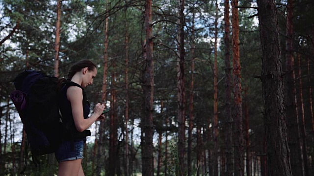 在美丽的野生森林里，背包女游客使用智能手机上的导航应用程序。旅游的概念视频素材