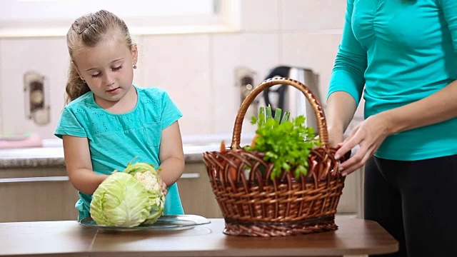 女孩帮助妈妈从篮子里拔菜视频素材