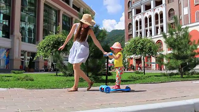 一个阳光明媚的夏日，妈妈教孩子在公园里骑滑板车。全高清。1920 x1080视频素材