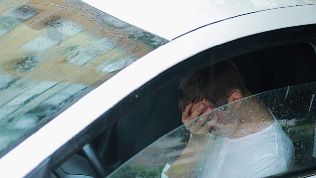 可悲的男人在车里哭。雨落在街上。人歇斯底里视频素材