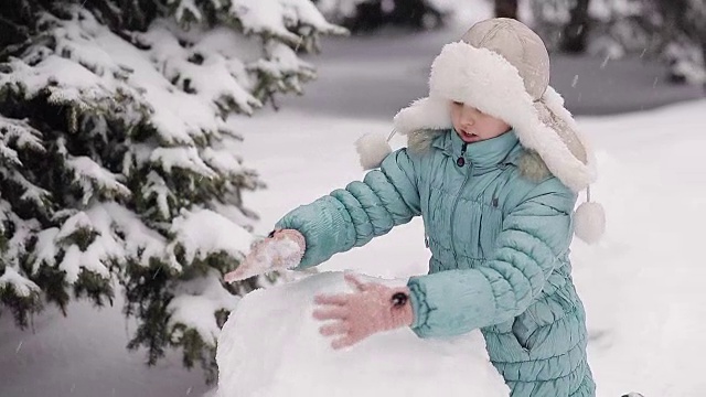 女孩冬天在雪地里堆雪人。视频素材