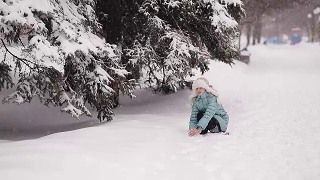 小女孩在冬季公园堆雪人。雪花从天上飘落。视频素材