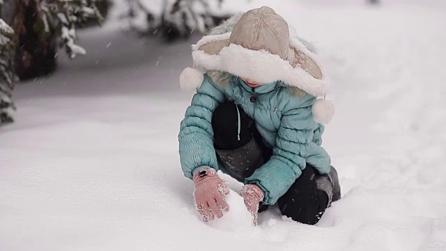 小女孩在冬季公园堆雪人。雪花从天上飘落。视频素材