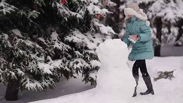 女孩冬天在雪地里堆雪人。视频素材