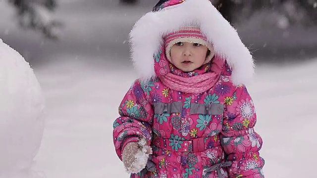 女孩冬天在雪地里堆雪人。视频素材