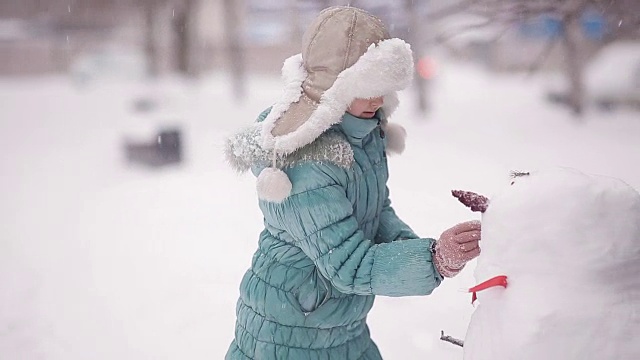 女孩冬天在雪地里堆雪人。视频素材