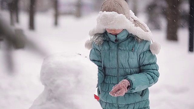 女孩冬天在雪地里堆雪人。视频素材