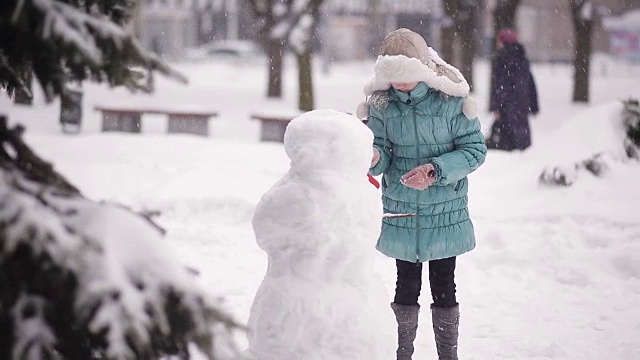 女孩冬天在雪地里堆雪人。视频素材