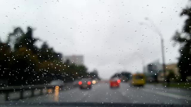 在雨中开车沿着城市街道，水滴落在挡风玻璃上，时间流逝视频素材