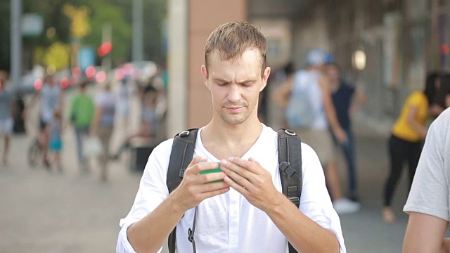 一个男人在大街上打手机。年轻人用智能手机发短信。视频素材