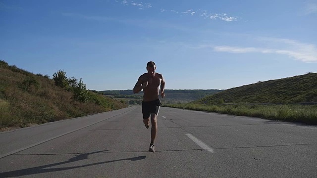 短跑运动员在高速公路上慢跑。男子运动运动员夏季户外训练。年轻强壮的肌肉男锻炼在农村道路上锻炼期间。积极健康的生活方式。慢动作视频素材