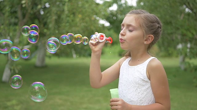 一个可爱的女孩在花园里吹泡泡。视频素材