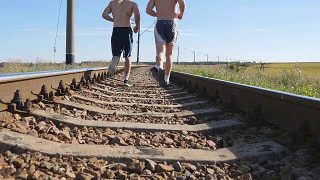 两个人在铁轨之间奔跑。短跑运动员在铁路枕木上慢跑。夏季户外运动运动员的腿部训练。积极健康的生活方式。特写镜头视频素材