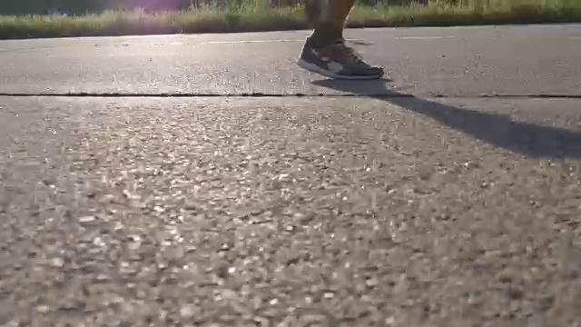 壮汉的脚在夏天的路上奔跑。日落时分，男性在乡村路线上进行慢跑训练。年轻人正在一条空荡荡的柏油路上训练。近距离在户外运动视频素材