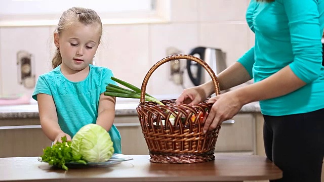 女孩帮助妈妈从篮子里拔菜视频素材