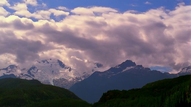 宽镜头时间流逝白色蓬松的云在蓝天与绿色的山在前景/不列颠哥伦比亚视频素材