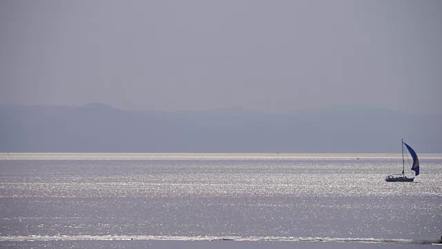 平静的海面，小帆船和一对喷气式飞机在天空中滑翔。日落视频素材