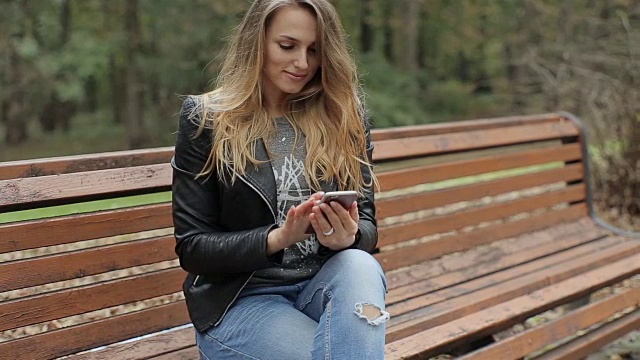 女孩使用手机-智能手机在公园的长凳上视频素材