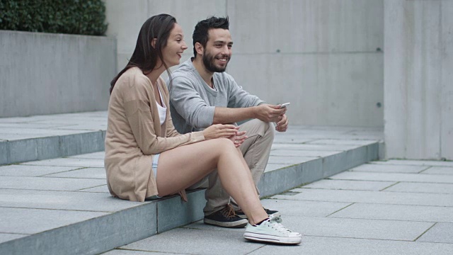 年轻的快乐微笑的男人和女人正坐在户外的台阶上交流。视频素材