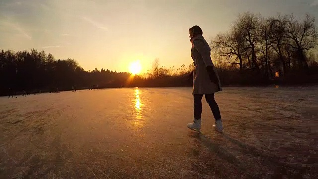 近景:日落时分，年轻女子在当地公园的大池塘上快速滑冰视频素材